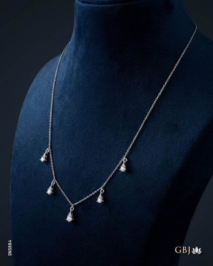A delicate silver-toned necklace with five small dangling floral clusters, displayed on a dark navy blue velvet jewelry bust. The brand logo 'GBJ' is visible in the bottom right corner.