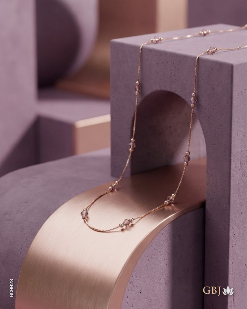 A delicate rose gold chain necklace with small bead and floral details draped over modern geometric display blocks in a studio setting.